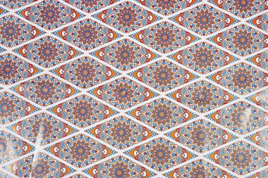 Bu resim kırmızı, mavi ve turuncu renkli renkli mandala tasarımları ile canlı ve karmaşık bir geometrik desen içerir. Tekrarlayan elmas şekilleri görsel olarak çekici ve simetrik 