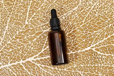 Altın çizgili yaprak dokusunda kürsüde duran boş kehribar rengi cam esaslı yağ şişesi. Doğal kozmetik ile cilt bakımı kavramı