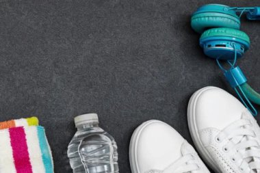 Sağlıklı yaşam tarzı, spor veya atlet ekipmanları seti: mavi kablosuz kulaklık ve havluyla bir şişe su, gri arka planda spor ayakkabıları