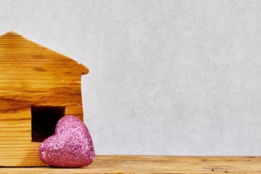 Tahta masa üzerinde küçük parlak bir kalbi olan küçük ahşap bir ev modeli. Mülk almayı planlıyorlar. En iyi konsepti seç.