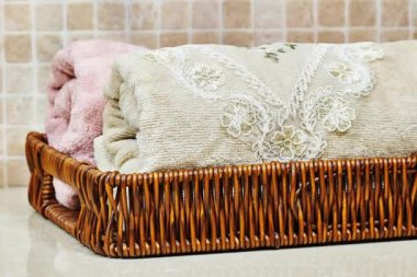 Hasır sepetin içinde havlular, banyo süsü vazosunda otlar.