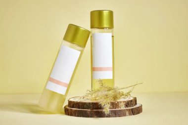 Tahta tabağa yaslanmış iki kozmetik şişesi ve kuru bitkiler boş etiketler gösteriyor.