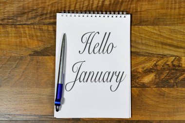 Tahta bir masada 'Merhaba Ocak' mesajını gösteren zarif bir defter.