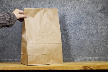 Teslimat servisi konsepti. Eko-el sanatları yapan bir kadın yemek paketini ahşap masada tutuyor. Paketleme şablonu oluşturur. Boşluğu kopyala