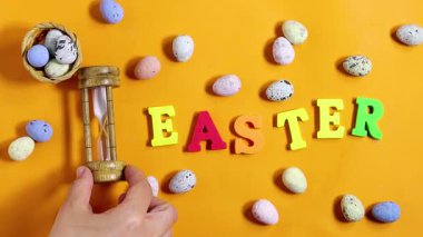 Paskalya kutlaması konsepti boyalı dekoratif yumurtalar, temalı harfler parlak turuncu arka planda Paskalya ve kum saati. 