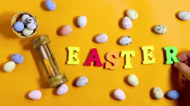 Paskalya kutlaması konsepti boyalı dekoratif yumurtalar, temalı harfler parlak turuncu arka planda Paskalya ve kum saati. 