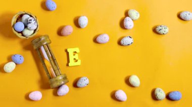 Paskalya kutlaması konsepti boyalı dekoratif yumurtalar, temalı harfler parlak turuncu arka planda Paskalya ve kum saati. 