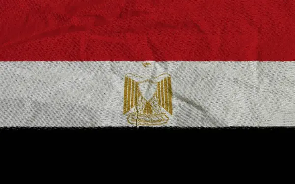 Altın kartal amblemiyle süslenmiş kırmızı, beyaz ve siyah yatay çizgilere sahip Mısır bayrağı, akan bir kumaş yüzeyde sergilenmektedir.