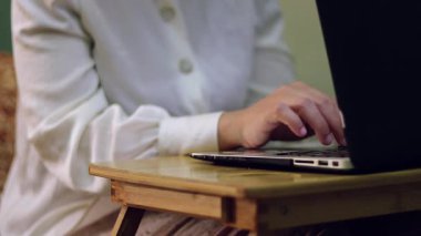 Çalışma ortamında üretkenliği ve modern teknolojiyi vurgulayan, ahşap bir masanın üzerine dizüstü bilgisayarda yazı yazan ellerin yakın çekim görüntüsü