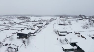 Ahşap evlerin çatıları karla kaplıydı. Şarjör. Şiddetli bulutlu arka planda küçük bir kış köyü