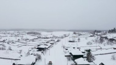 Ahşap evlerin çatıları karla kaplıydı. Şarjör. Şiddetli bulutlu arka planda küçük bir kış köyü