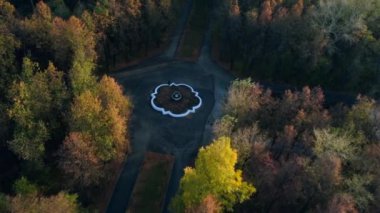 Sonbahar ormanındaki çeşme ve yolların üst manzarası. Şarjör. Yollar fıskiyeyle kesişiyor. Bulutlu bir günde sonbahar ormanında çeşmeyle kesişen yollar. 
