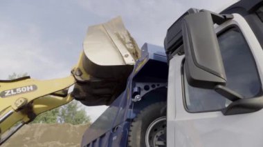 Almanya - Berlin, 20 Kasım 2022: Kazıcı inşaat alanında faaliyet gösteriyor. Sahne. Kazıcı sarı renkli kovayı çevirip kumla dolduruyor, kamyonu kumla dolduruyor.