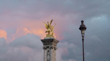 Fransa, Paris - 24 Temmuz 2022: Bulutların arkasındaki kulede altın heykel. Başla. Renkli akşam bulutlarının arka planında altın heykeli olan güzel bir manzara. Alexander 'ın Altın Heykeli