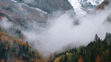 Kayalık karlı yamaçta canlı bulutlar. Yaratıcı. Dağların eteğindeki renkli ağaçlar