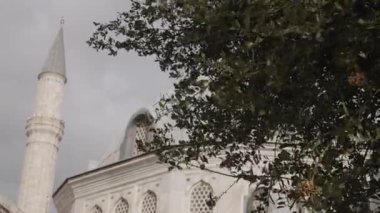 Bulutlu bir arka planda cami minaresi. Başla. Yaz yeşili ağaçlar ve cami binası