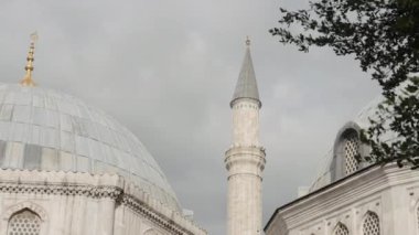 Bulutlu bir arka planda cami minaresi. Başla. Yaz yeşili ağaçlar ve cami binası