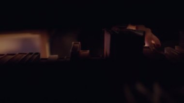 Parmaklar kitaplıkta hareket ediyor. Stok görüntüleri. Yakın plan karanlık raftan gizemli bir kitap seçer. Gizemli eliyle kitaplıkta yanıp sönen ışık.. 