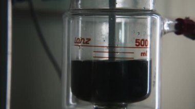 Laboratuvar matarasında dönen koyu sıvı. Stok görüntüleri. Kimyasal deney için kurulumuyla birlikte matarada fokurdayan sıvı. Sıvı ile yapılan kimyasal deney matara ve döndürme veya ısıtma. 