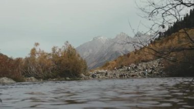 Dağların ve ormanların arka planına karşı sakin bir gölet. Yaratıcı. Sonbahar ağaçları ve yüksek dağlarla dolu parlak bir manzarayla aydınlık bir gündüz gökyüzünün arka planına karşı. Yüksek kalite