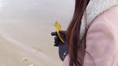 Ellerinde sarı bir ağaç olan, sıcak giysili bir kadının omzunun üstünden bak. Stok görüntüleri. Kumsalda yürüyen kadın köprüye doğru