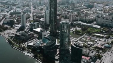 Yükseltilmiş yaz şehrinin helikopter görüntüsü. Stok görüntüleri. Gökdelenleri ve evleri olan şehir merkezinin güneşli manzarası ve turistlerin yürüdüğü küçük bir gölet. Yüksek kalite 4k görüntü