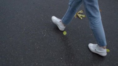 Islak asfalt üzerinde beyaz ayakkabılarla yürüyen adamın yakın çekimi. Stok görüntüleri. Islak asfaltta beyaz spor ayakkabılar. Adam ıslak asfaltta temiz beyaz ayakkabılar giyer.. 