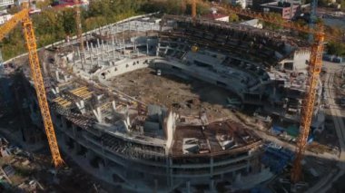 Şehirdeki büyük stadyumun en üst manzarası. Stok görüntüleri. Modern şehirde vinçleri olan stadyum inşaatı yapılıyor. Güneşli bir günde vinçli stadyum inşaatı. 