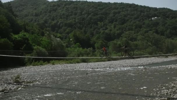 ハイカーは 野生の美しい川を横断する橋の上に自転車で歩きます クリエイティブ 熱帯雨林を探索する若いカップル — ストック動画