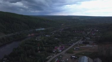 Helikopterden alınan bulutlu hava manzarası. Şarjör. Küçük yerleşim binaları ve bir nehri olan küçük bir köyün üzerindeki gri gökyüzü. Yüksek kalite 4k görüntü