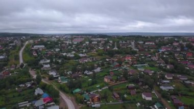 Helikopterden alınan bulutlu hava manzarası. Şarjör. Küçük yerleşim binaları ve bir nehri olan küçük bir köyün üzerindeki gri gökyüzü. Yüksek kalite 4k görüntü