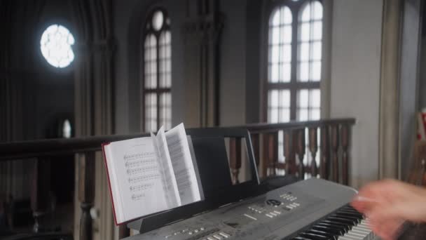 带着乐谱和钢琴的人行动 人类翻阅着合成器上的音乐书籍 音乐人在教堂合成器上的特写 — 图库视频影像