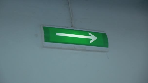 壁に緑色の矢が輝いています クリップ 出口を示すために緑色の背景ライトに矢印を付けます 建物の壁の緑の背景で避難出口の矢が光る — ストック動画
