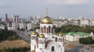 Açık havada altın kubbeleri olan ortodoks beyaz kilise binası. Tock görüntüleri. Hristiyanlık dini, katedral ya da tapınak. Arka planda büyük bir yaz şehri var.