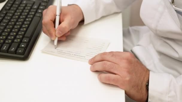 男性医師の手が紙に処方箋を書いている クリップ コンピュータキーボード 病気治療プロトコルを搭載した医師のデスク — ストック動画