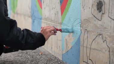 Erkek ergen el boya fırçasıyla mavi renkte bir duvar boyuyor. Şarjör. Yetenekli öğrenci sokak sanatı nesnesi yapıyor