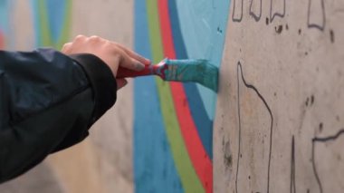 Duvarda grafiti sanatçısı resmi, dış görünüş. Şarjör. Duvarı boyamak için fırça ve boya kullanarak erkek elini kapat.