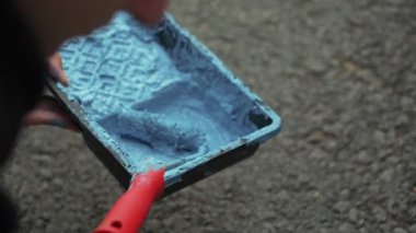 Bilinmeyen kişi elinde mavi boya ve silindirli plastik tepsi tutuyor. Şarjör. Tamir işleri ve konut koşullarının iyileştirilmesi