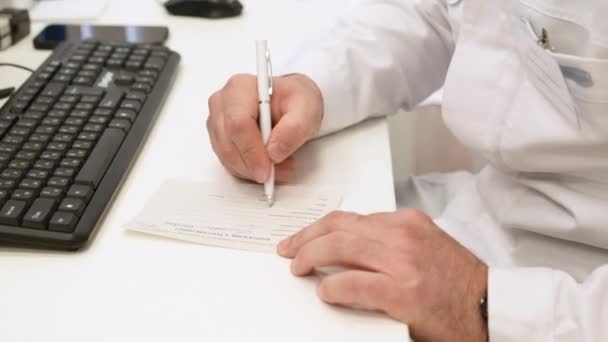 男性医師の手が紙に処方箋を書いている クリップ コンピュータキーボード 病気治療プロトコルを搭載した医師のデスク — ストック動画