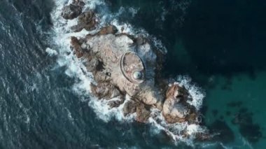 Deniz feneri olan kayalık güzel bir pelerin manzarası. Şarjör. Mavi dalgalı ve kayanın üzerinde deniz feneri olan sinematik bir manzara. Güneşli bir günde dalgalı deniz feneriyle Rocky Pelerin. 