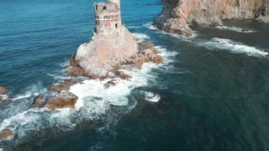 Güneşli bir günde terk edilmiş deniz fenerinin en üst manzarası. Şarjör. Mavi deniz dalgalı kayalıklarda terk edilmiş deniz feneri. Kayalara çarpan deniz dalgalarının arka planında güzel bir deniz feneri. 
