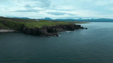 Bulutlu bir günde dağların arkasındaki kayalık kıyı manzarası. Şarjör. Bulutlu bir yaz gününde kayalık kıyıları olan güzel kuzey manzarası. Dağ ufukları ve bulutlu gökyüzü ile kayalık okyanus kıyıları. 