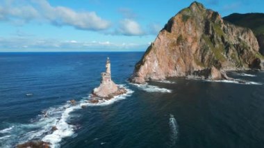 Deniz feneri olan kayalık güzel bir pelerin manzarası. Şarjör. Deniz dalgalı kayalık pelerin ve deniz feneri manzarası. Güneşli bir yaz gününde, deniz feneriyle terk edilmiş Rocky Cape.