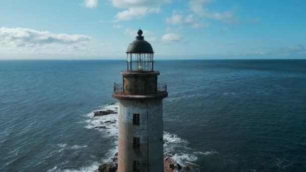 阳光明媚的日子 可以俯瞰大海中被遗弃的灯塔 废弃的灯塔在岩石上 伴随着蓝色的海浪 在海浪冲撞岩石的背景下美丽的灯塔 — 图库视频影像