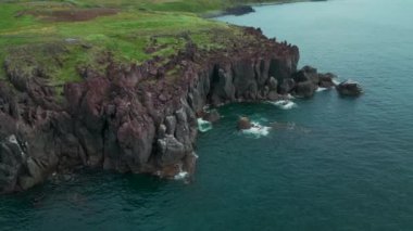 İzlanda 'daki kayalıklar ve manzara, hava manzarası. Şarjör. Gök mavisi deniz ve kıyının dik kayalık yamacı