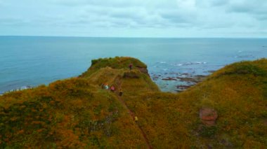 Kaya üzerinde turistlerin olduğu güzel deniz manzarası. Şarjör. Kayalık sahilin kenarına ilham verici bir yaklaşım. Uçuruma bakan deniz ufkunda turistlerin güzel manzarası. 