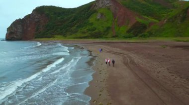 Dağ manzaralı deniz manzaralı insanlar. Şarjör. Sahilde yürüyen insanlar ve bulutlu bir günde inanılmaz dağlar. Bulutlu bir günde okyanus kıyısında yürü. 