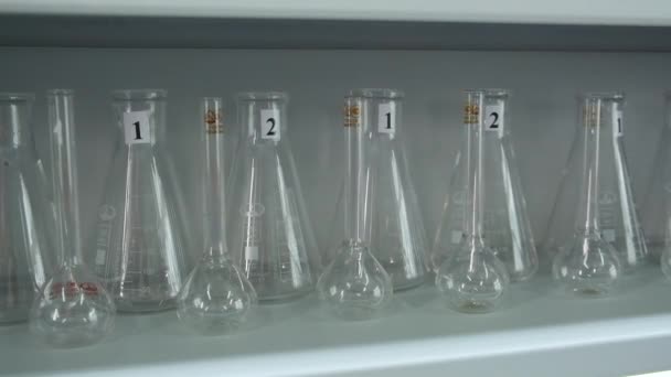 架子上的多个实验室瓶 可随时使用 手拿着一只空玻璃瓶手套的医生或科学家的手 — 图库视频影像