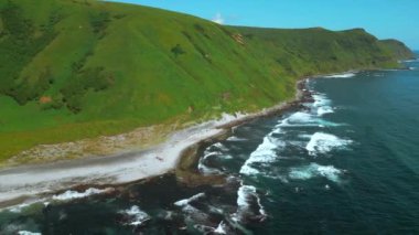  Vahşi doğa, denize uzanan sarp yeşil yamaçlı yeşil dağlar. Şarjör. Mavi dalgaların havası volkanik kayalarda kırılır.