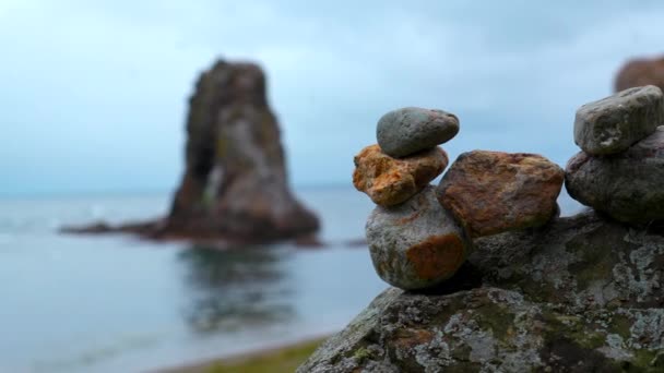 在海滩上堆放岩石的特写镜头 石头堆放在海洋岩石模糊的背景上 堆放在炮塔中的石子 耸立在阴沉沉的大海中 — 图库视频影像
